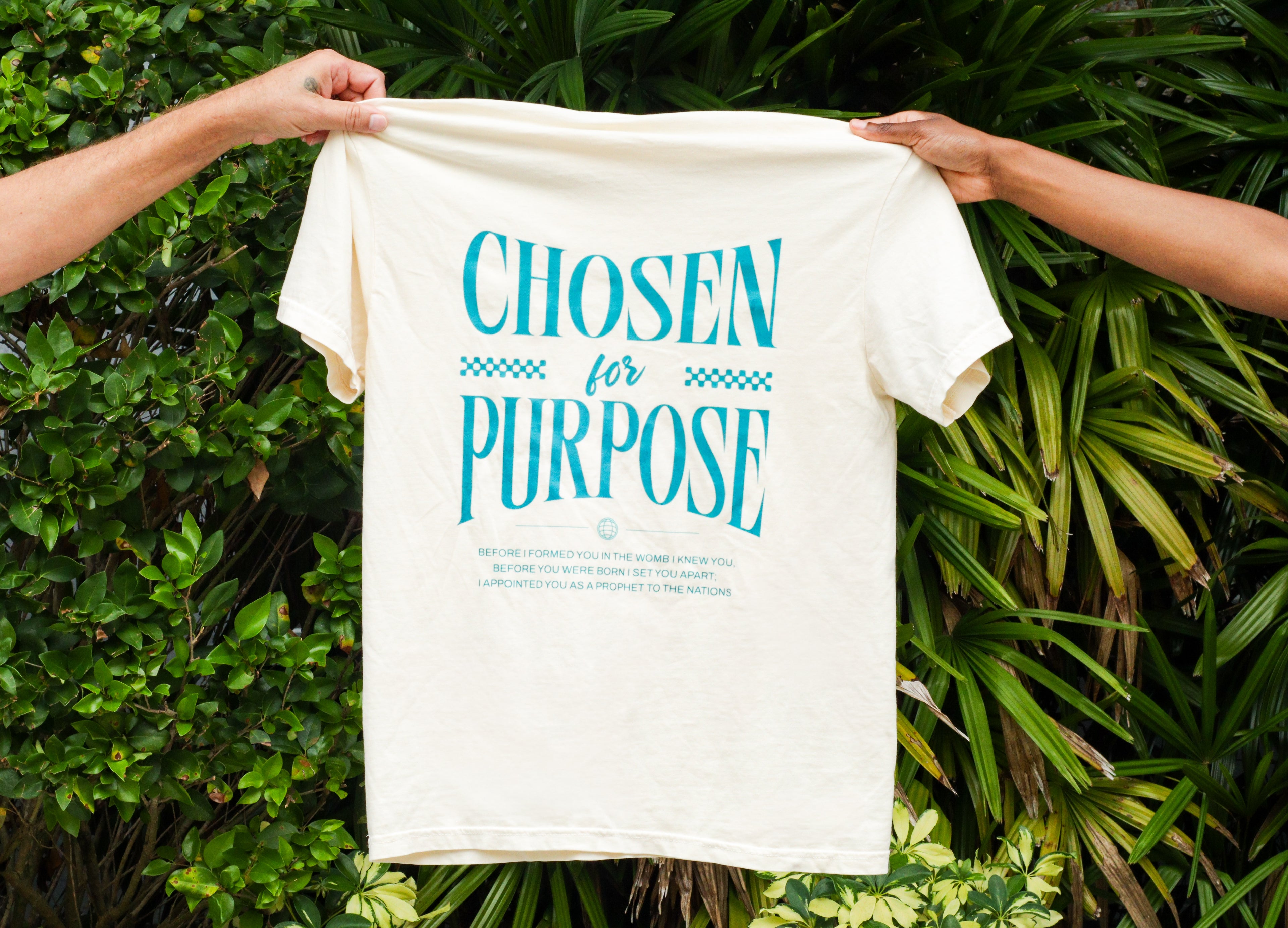 White t-shirt with 'Chosen for Purpose' text held by two people against a green leafy background